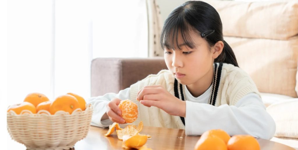 こたつでみかんを食べる少女